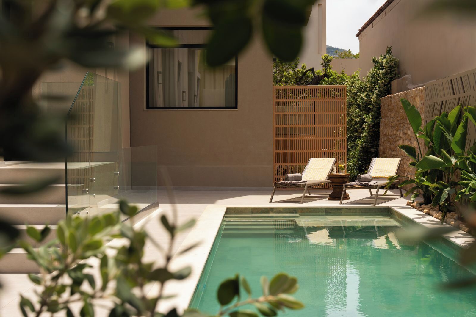 Un espace piscine extérieur moderne, doté de deux chaises longues, d’une clôture en bois et d’une enceinte en verre.