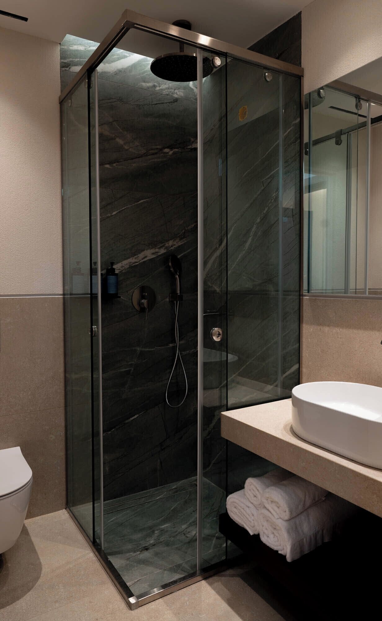 A modern bathroom with a glass-enclosed shower, a white sink, and a marble-tiled wall.