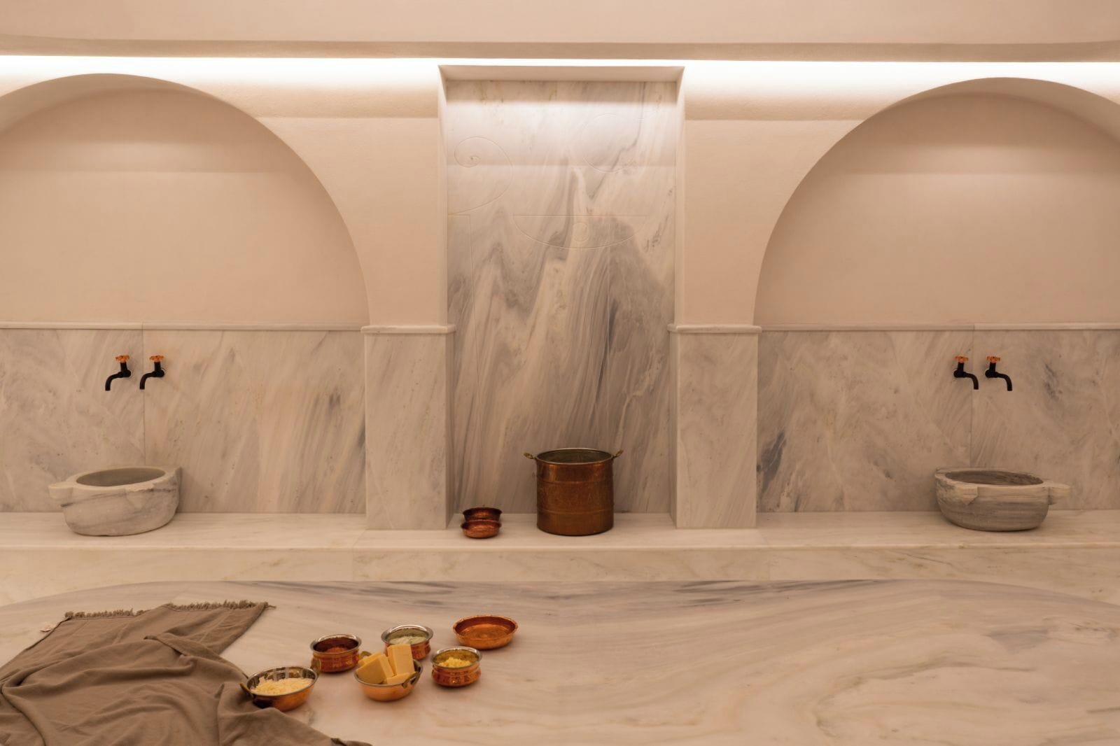 A spa room with two marble sinks, a central hot tub, and various toiletries on the floor.