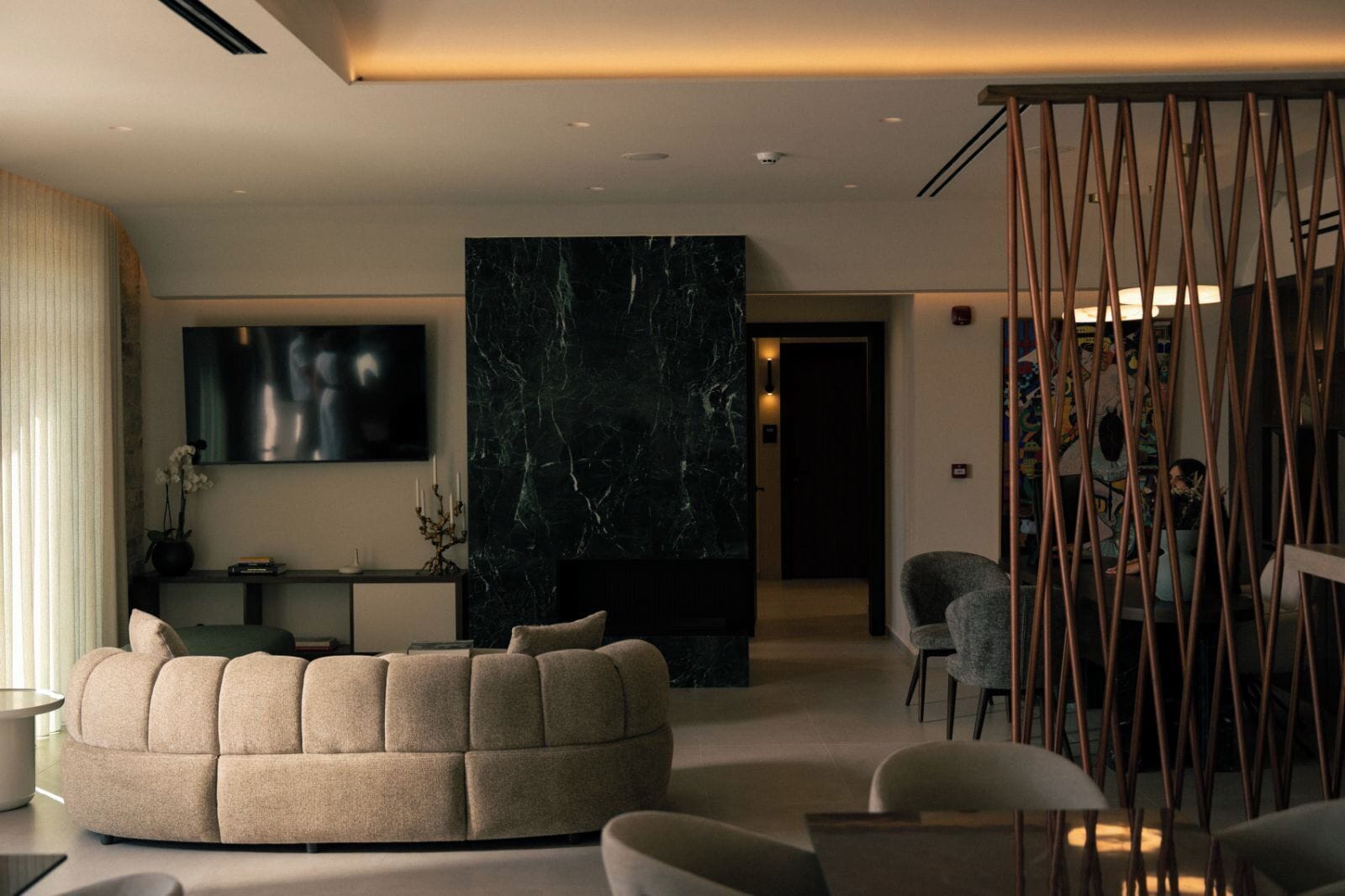 A modern living room with a sofa, chairs, a TV, and a decorative wall.