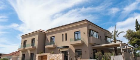 A modern two-story house with a stone facade, multiple balconies, and a clear blue sky.