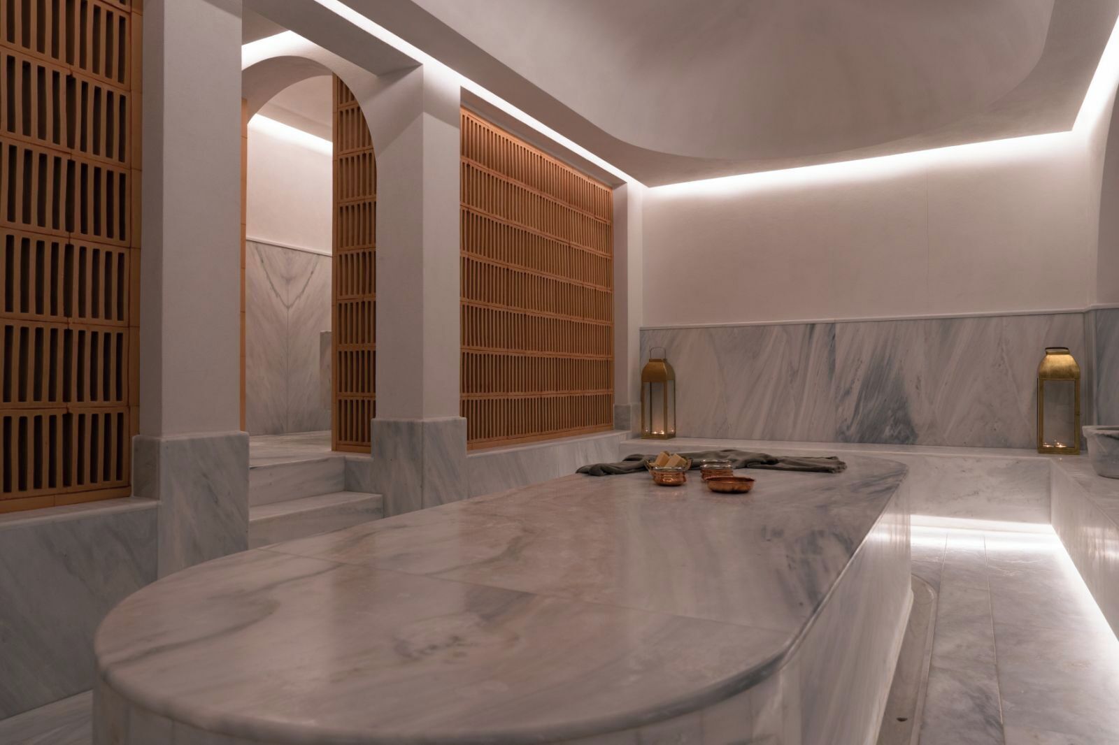 A modern bathroom with a marble vanity, wooden slatted doors, and a marble floor.
