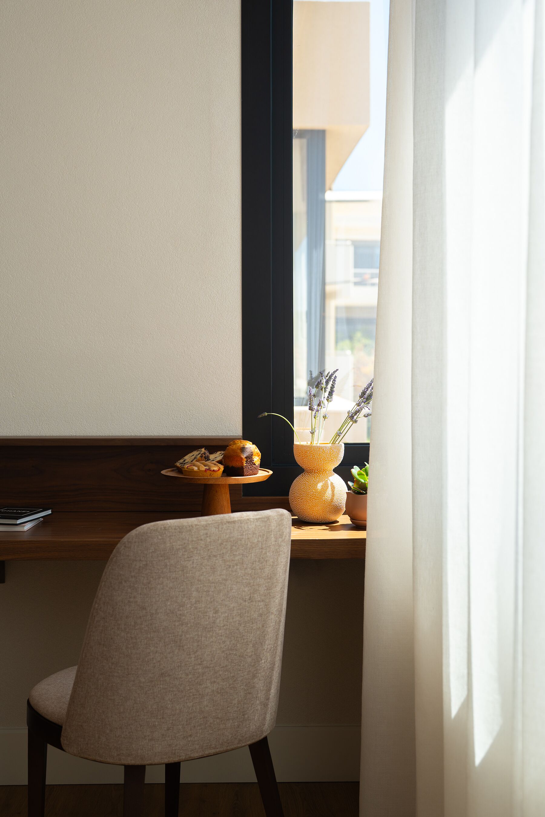 A chair, a small table with a vase of flowers, and a window with curtains.