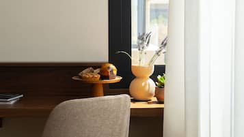 A chair, a small table with a vase of flowers, and a window with curtains.