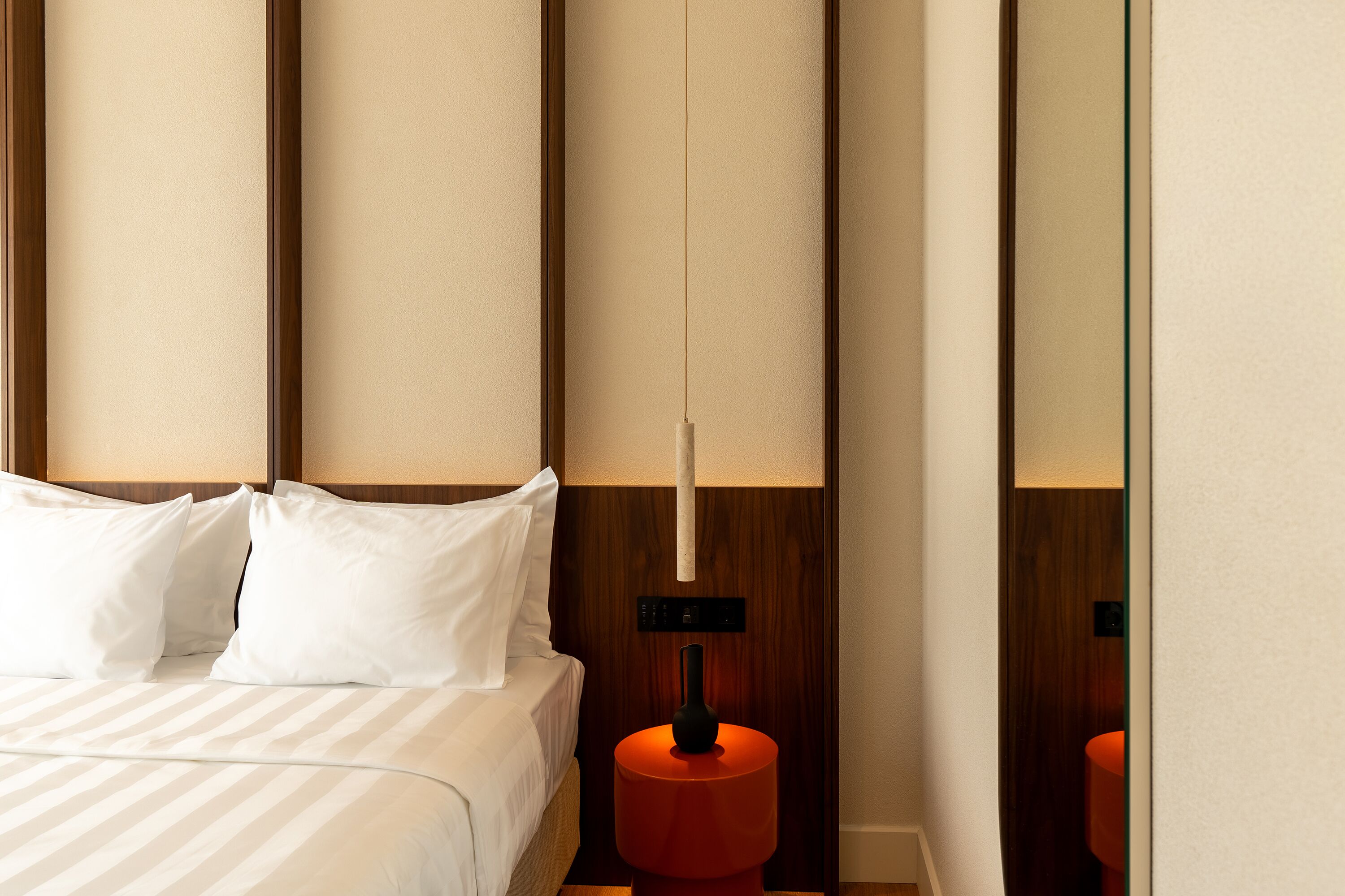 Una habitación de hotel con cama, mesita de noche, lámpara y espejo.