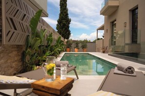 Zona de piscina con una silla de descanso, una mesa con un vaso de agua y plantas en macetas.