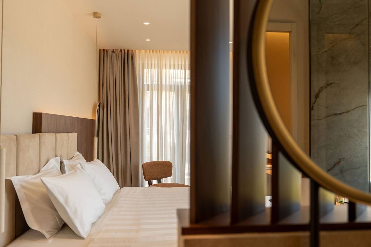 A hotel room with a bed, a chair, a television, and a large mirror.