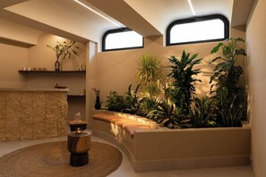 Un cuarto de spa con un banco de piedra, un taburete de madera y diversas plantas.