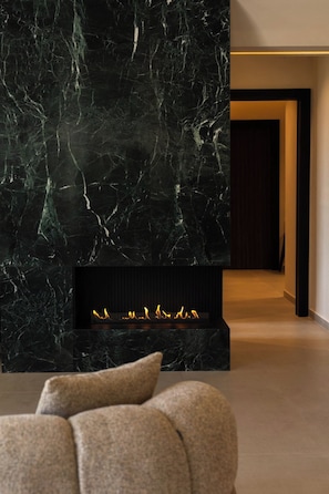 Una sala de estar moderna con chimenea de mármol oscuro, un sofá y un pasillo que lleva a una puerta.