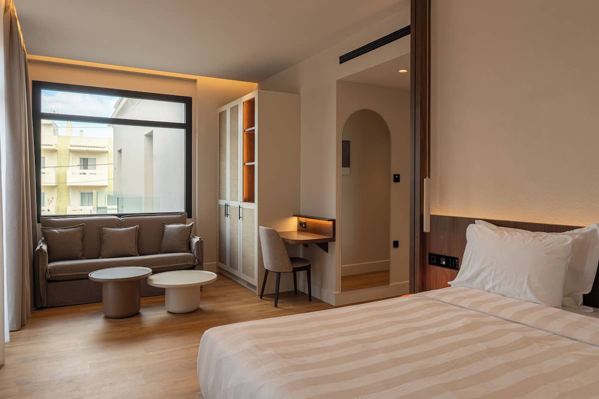 A hotel room with a bed, a sofa, a desk, and a chair.
