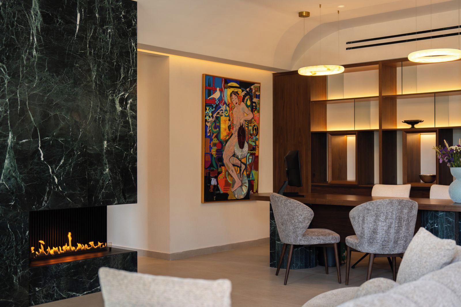 A modern interior with a marble fireplace, a colorful abstract painting, and a dining area with contemporary chairs.