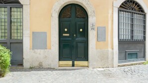 En bygnings facade med en grøn dør i to fløje, et vindue med en metalgitter og et tremmevindue.