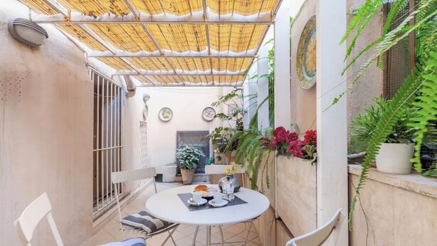 En overdækket terrasse med et bord til to, stole og potteplanter.