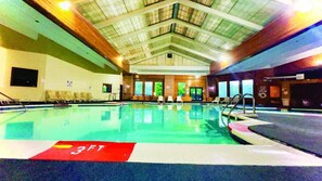 Una piscina interior con indicador de profundidad de 3 pies, techo de madera y ventanas.