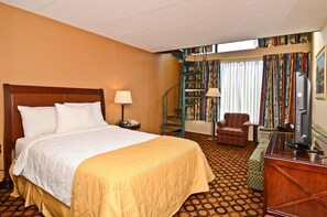 Habitación de hotel con cama, escritorio, silla, televisor, lámpara, escalera y ventana con cortinas.
