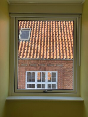 Ein Fenster mit Blick auf ein Backsteingebäude, ein Ziegeldach und ein kleines Fenster darüber.
