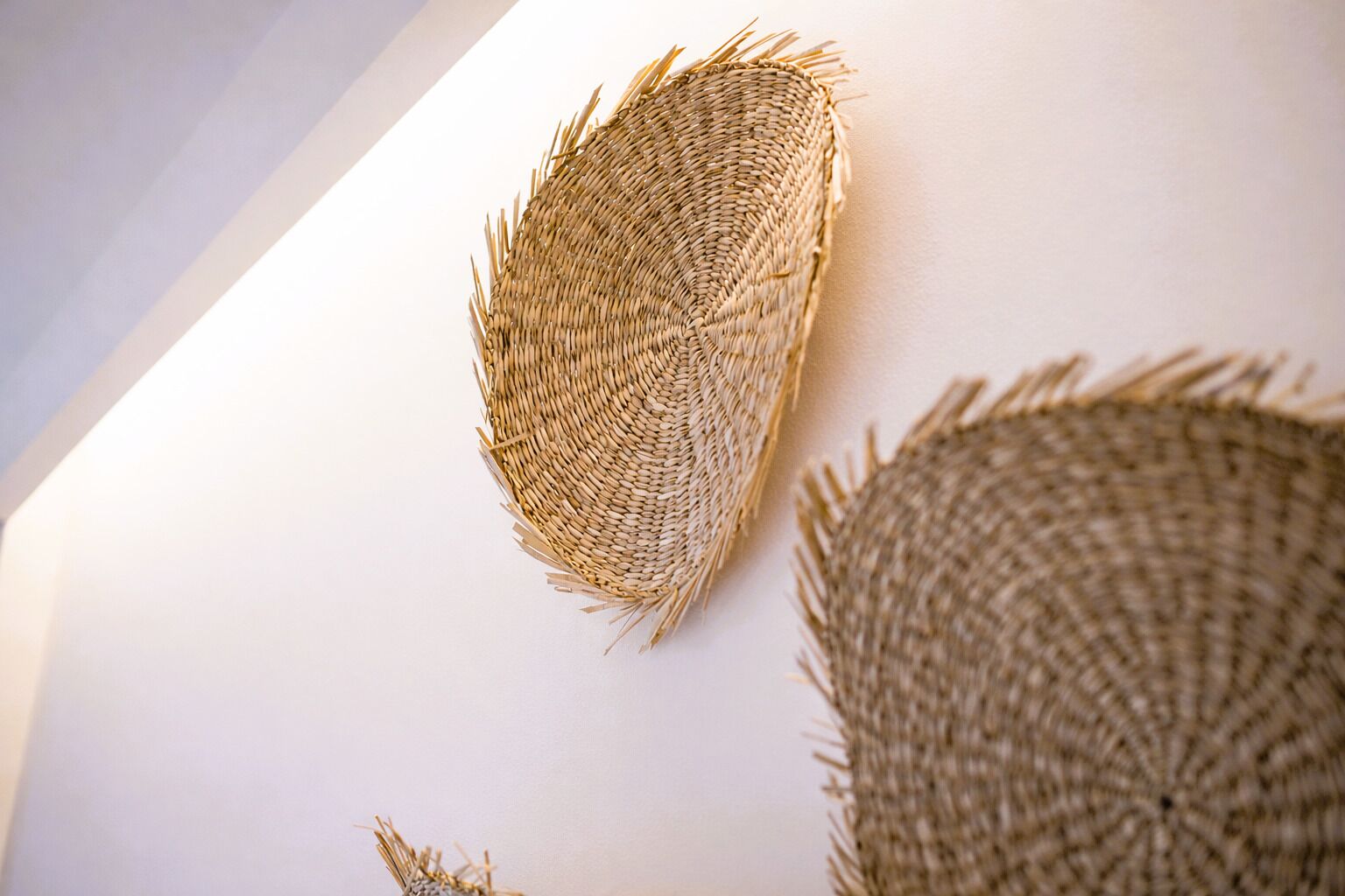 A wall with woven wall art, a ceiling with a sloped design, and a partial view of a room.