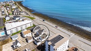 An aerial view of a coastal residential area with buildings, a road, and the ocean. - Oceanfront Apartment w/ 2 Bedroom + den & pool access (Hampton)
