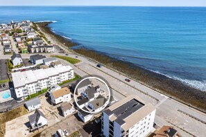 An aerial view of a coastal residential area with buildings, a road, and the ocean. - Oceanfront Apartment w/ 2 Bedroom + den & pool access (Hampton)