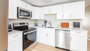 A modern kitchen with white cabinets, stainless steel appliances, and a built-in microwave. - Oceanfront Apartment w/ 2 Bedroom + den & pool access (Hampton)