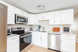 A modern kitchen with white cabinets, stainless steel appliances, and a built-in microwave. - Oceanfront Apartment w/ 2 Bedroom + den & pool access (Hampton)