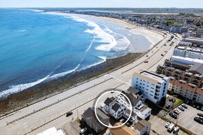 Luftaufnahme einer Küstenregion mit Strand, einer Straße und Gebäuden.