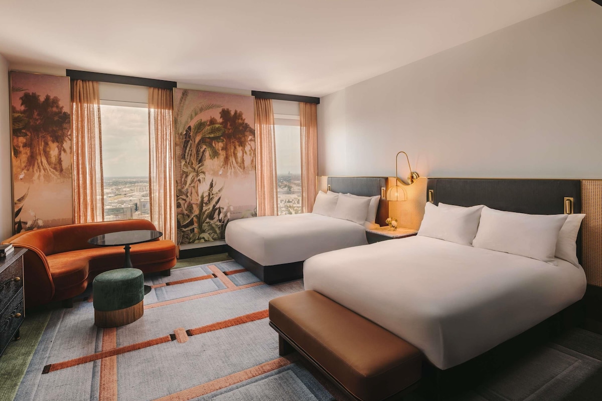 A hotel room with two beds, a sofa, a small table, and a view of the city.