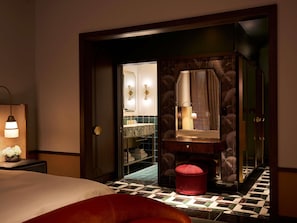 A hotel room with a bed, a nightstand, a mirror, a vanity with a sink, and a red ottoman. - Fairmont New Orleans (Opening November 2026) (New Orleans)