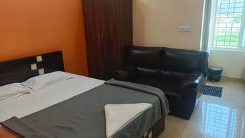 Un dormitorio con cama, armario, sofá de cuero, ventana y un cubo de basura.