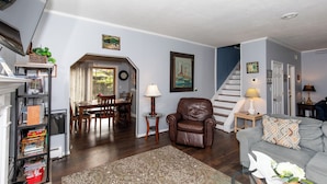 A living room with a fireplace, a sofa, a coffee table, and a dining area with a table and chairs. - Family Cottage Near Cedar Point and Sports Center! (Huron)