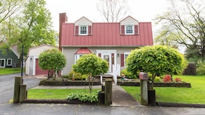 A two-story house with a red roof, a front porch, and a well-maintained garden. - Family Cottage Near Cedar Point and Sports Center! (Huron)