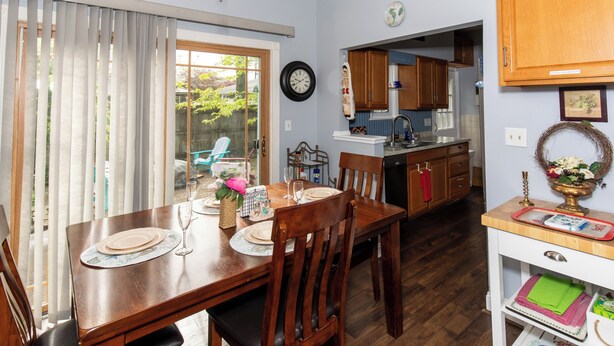 A dining area with a table set for four, a kitchen in the background, and a view of the outdoors through a sliding door. - Family Cottage Near Cedar Point and Sports Center! (Huron)