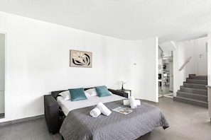 Una habitación de hotel moderna con una cama, una mesita de noche, un cuadro y una escalera.