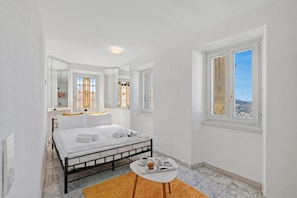 A bedroom with a bed, a small table with a tray, a window with a view, and a mirror.