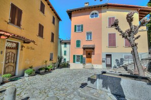 A cobblestone street with buildings featuring wooden shutters and a stone wall with a tree. - Charm Apartments (Lugano)