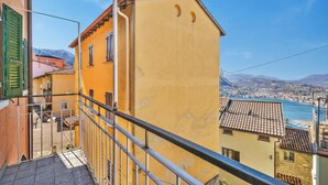 Un edificio amarillo con un balcón, barandilla metálica y vistas al agua y montañas a lo lejos.