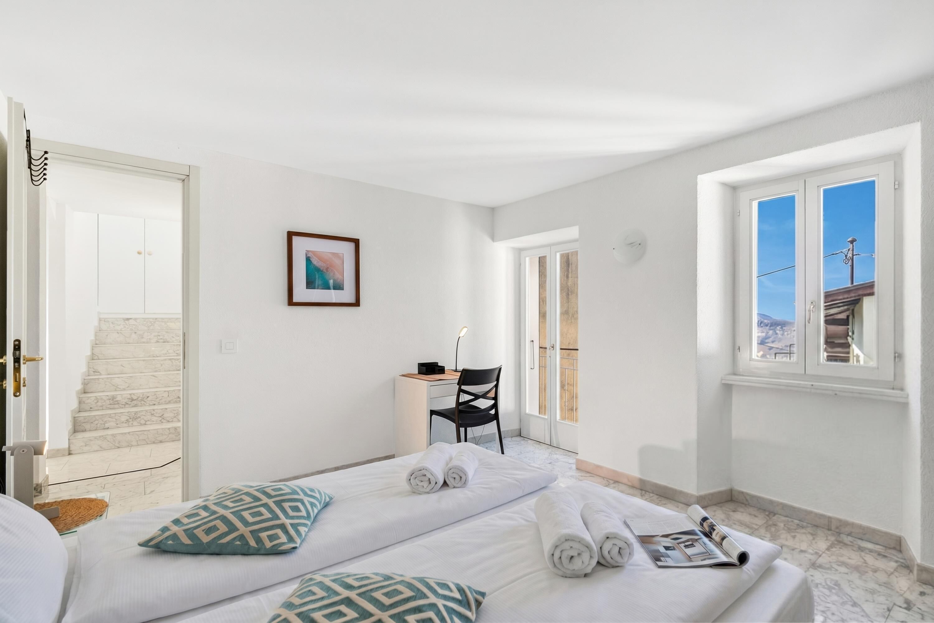 A hotel room with a bed, a desk, a chair, and a view of the outside.