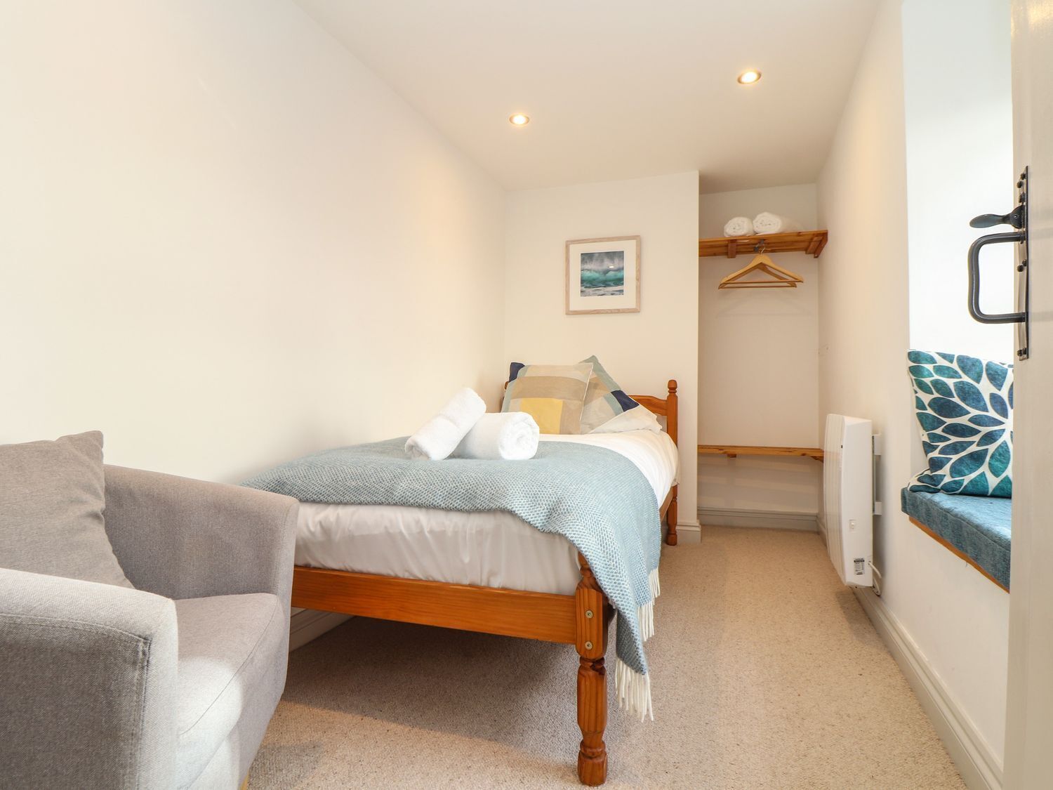 Un dormitorio con cama, una silla, un radiador y un perchero.