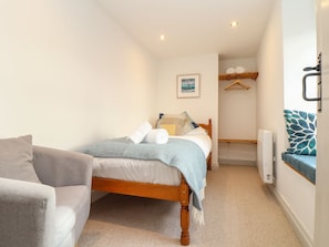 A bedroom with a bed, a chair, a radiator, and a hanging coat rack. - Ty Bryn (Marazion)