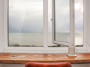 Una ventana con vista al mar, un escritorio de madera y una taza blanca en el alféizar.