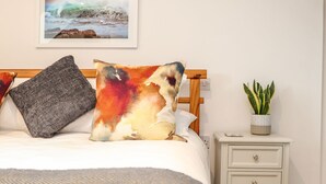 A bedroom with a bed, pillows, a nightstand, a potted plant, and a framed picture on the wall.