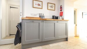A kitchen with grey cabinets, a wooden countertop, and two framed fish pictures on the wall.