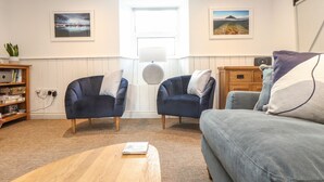 A living room with two dark blue armchairs, a grey sofa, a wooden coffee table, and a bookshelf.