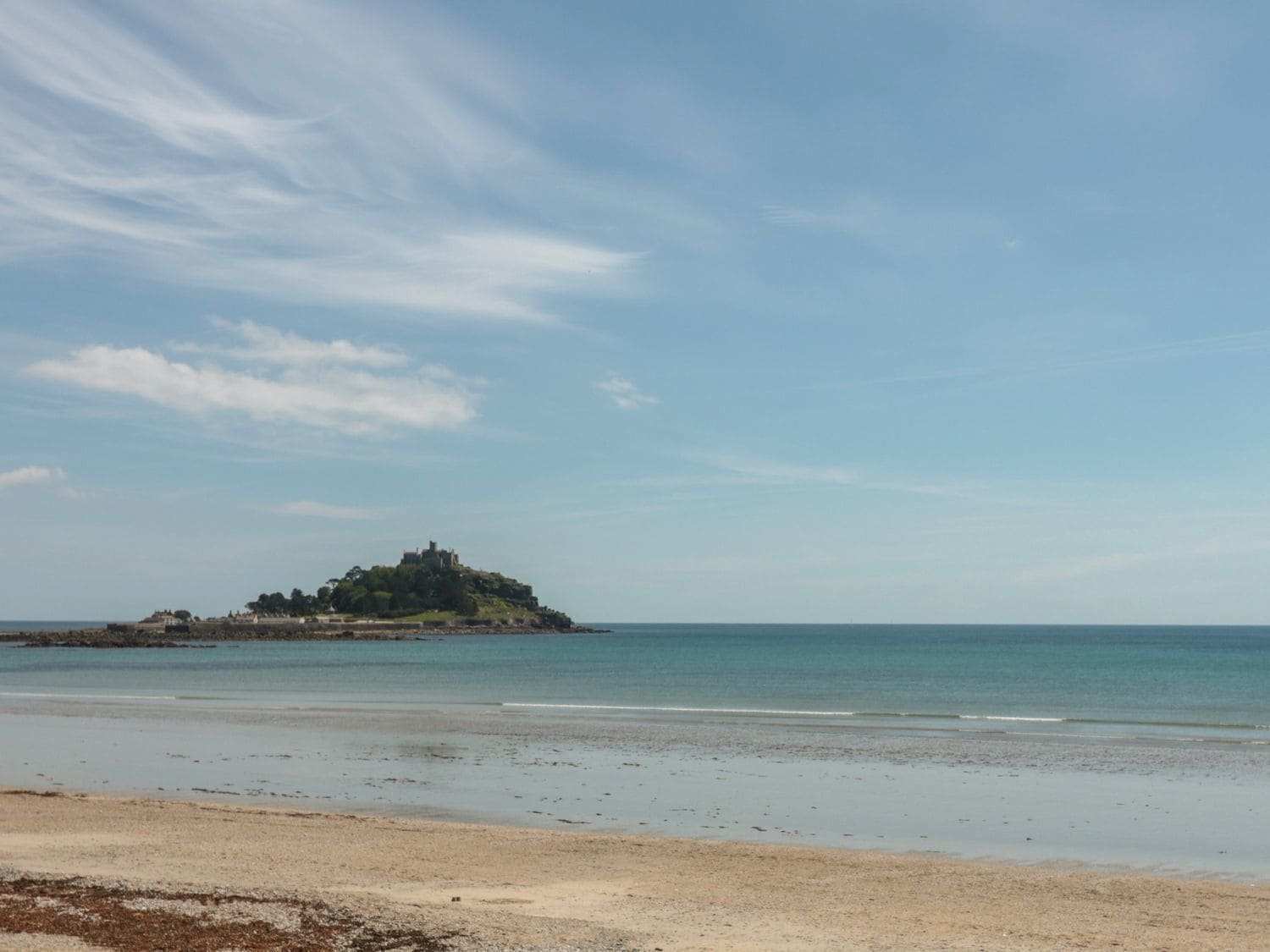 Ein Strand mit einer fernen Insel und blauem Himmel.