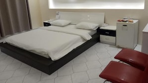 A modern hotel room with a bed, bedside tables, a small cabinet, and a red chair.