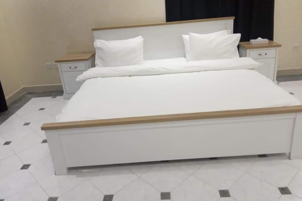 Ein Bett mit Holz-Kopfteil, weißer Bettwäsche und zwei Nachttischen mit Schubladen.