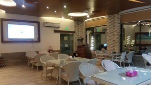 A conference room with glass tables and wicker chairs, air conditioning units, and a projection screen.