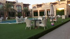 A courtyard with outdoor seating, a swimming pool, and a building with arched windows and a castle-like facade.
