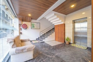 Un vestíbulo moderno con una escalera, un sofá, una planta en maceta y un extintor de incendios instalado en la pared.