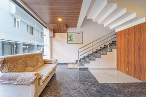 A modern interior with a sofa, a staircase, and a framed informational poster. - Treebo Regalia, Near Medical College & Pattom (Thiruvananthapuram)